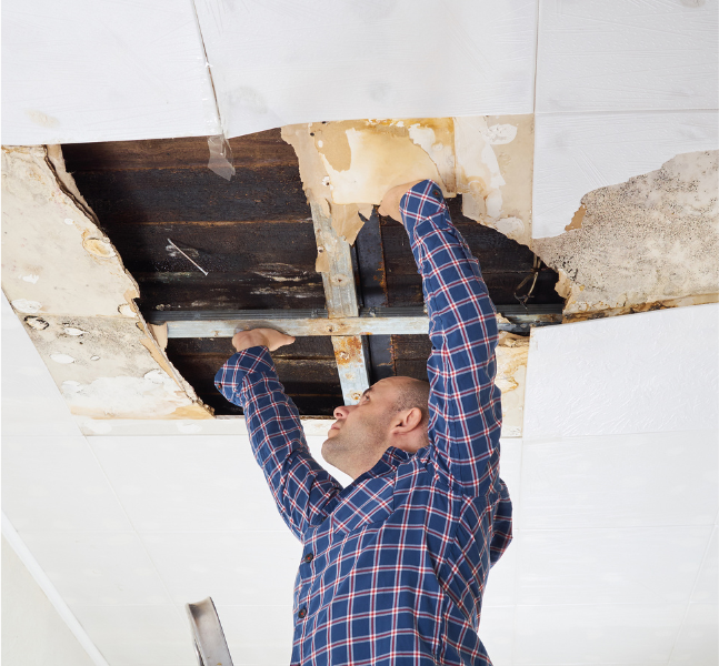 man looking at large hole in ceiling caused by water damage from leaking roof