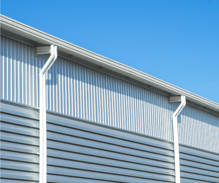 Close-up of corrugated metal siding and white rain gutters on a blue-sky building-facing wall.