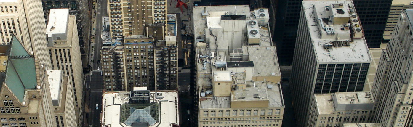 Bird's-eye view of a dense downtown with flat rooftops, HVAC units, and narrow streets between beige and gray skyscrapers.